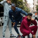 Three men pose in stylish active wear on a city street, embodying modern urban fashion.